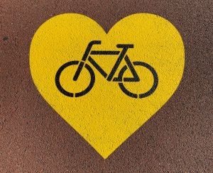 Yellow heart painted on road surface with image of a bike within the heart